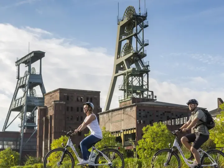Zwei Radfahrer genießen die Aussicht auf die beeindruckenden Fördertürme der Zeche Ewald, ein Symbol für Industriegeschichte und neuen Freizeitwert.