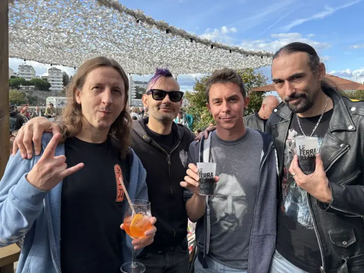 Quatre hommes, un groupe hollandais des années 80, posent avec des boissons. L'un fait un signe de rock.