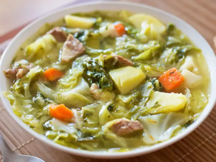 Un bol de soupe aux choux réconfortante, avec des morceaux de chou, pommes de terre, carottes et viande. Du pain frais à côté.