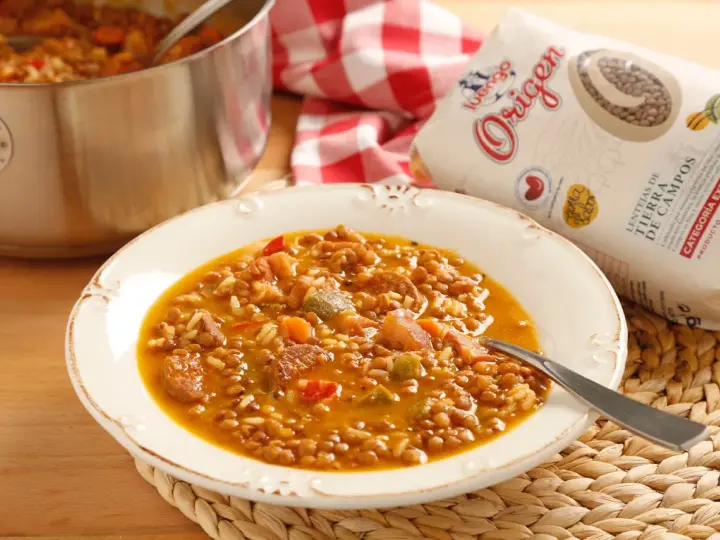 Plato de lentejas con arroz, chorizo y verduras. Una bolsa de lentejas "Origen" a un lado.