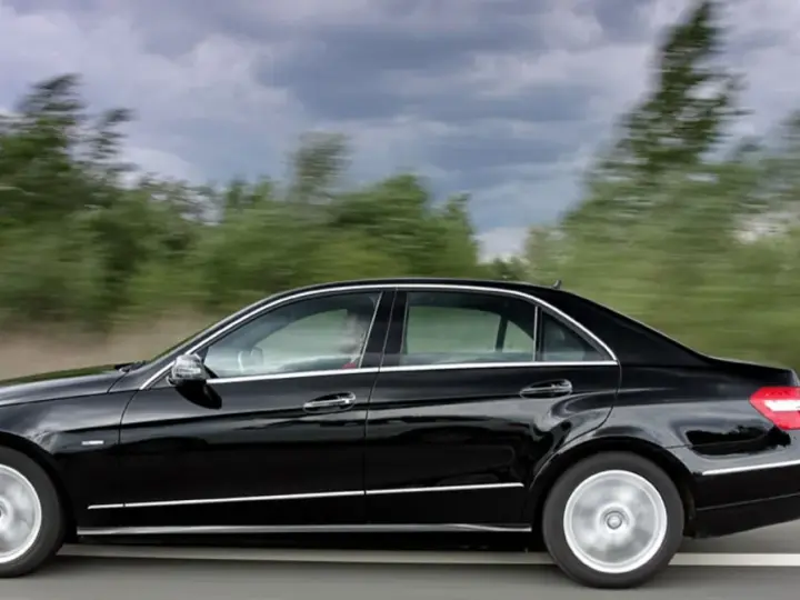 Czarny Mercedes E350 pędzi po drodze, mijając rozmyte zielone drzewa.