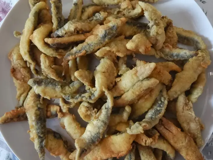 Un plato blanco lleno de boquerones fritos crujientes, listos para disfrutar.