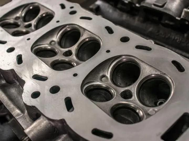 Nahaufnahme eines Zylinderkopfs eines Autos. Die Ventilsitze und die Bohrungen für die Zündkerzen sind sichtbar. Eine neue Kopfdichtung für das Auto wird bald montiert.