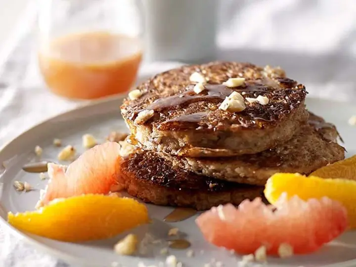 Pile de pancakes muesli, nappés de sirop et garnis de noix, accompagnés de quartiers d'agrumes.