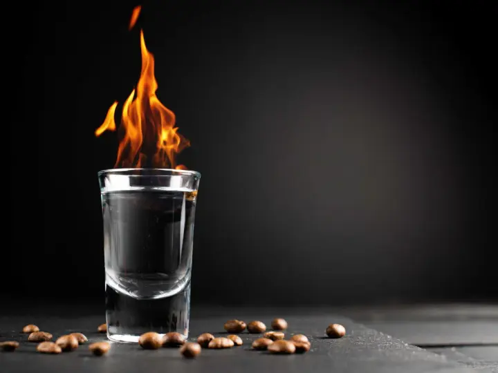 Ein Schnapsglas mit brennendem Sambuca und Kaffeebohnen. Die Flammen tanzen, ein Spektakel, das erklärt, warum brennt Sambuca.