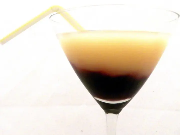 Dwukolorowy drink w kieliszku, z warstwą soku z czarnej porzeczki na dnie i jasnym płynem na górze, ozdobiony żółtą słomką.