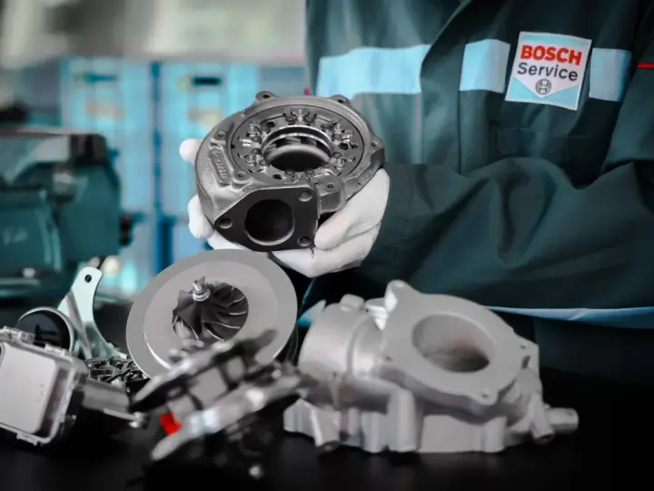Mechanik w rękawiczkach prezentuje turbosprężarkę i jej elementy. Widać wirnik, obudowę i części mechanizmu sterującego, jak zawór N75 podłączenie.