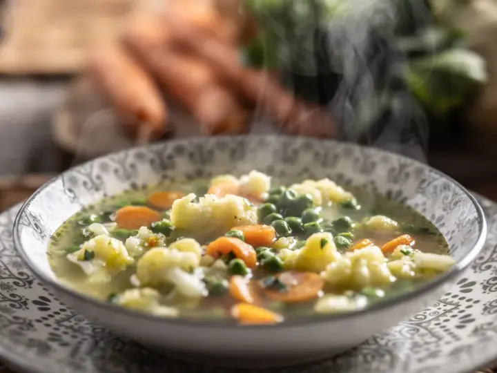 Zuppa fumante con cavolfiore, piselli e carote, arricchita da un tocco di panna da cucina per una cremosità avvolgente.