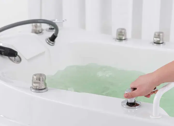 Dłoń reguluje strumień wody w wannie, przygotowując relaksujący masaż wirowy.