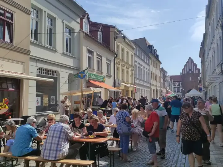 Menschen genießen ein Fest vor dem Kulturhaus Teterow. Viele sitzen an Tischen, essen und unterhalten sich.