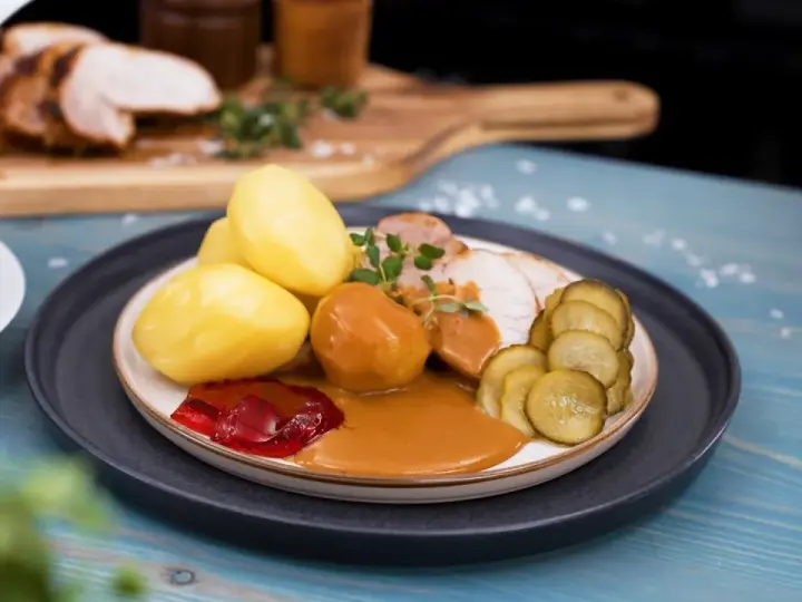 En tallrik med skivad ytterfile i sockerkaksform, potatis, sås, gelé och gurka.