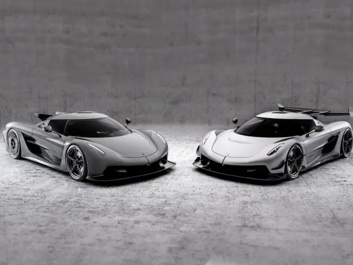 Dwa lśniące Koenigsegg Jesko, jeden szary, drugi srebrny, stoją obok siebie na betonowym tle, gotowe do wyścigu.