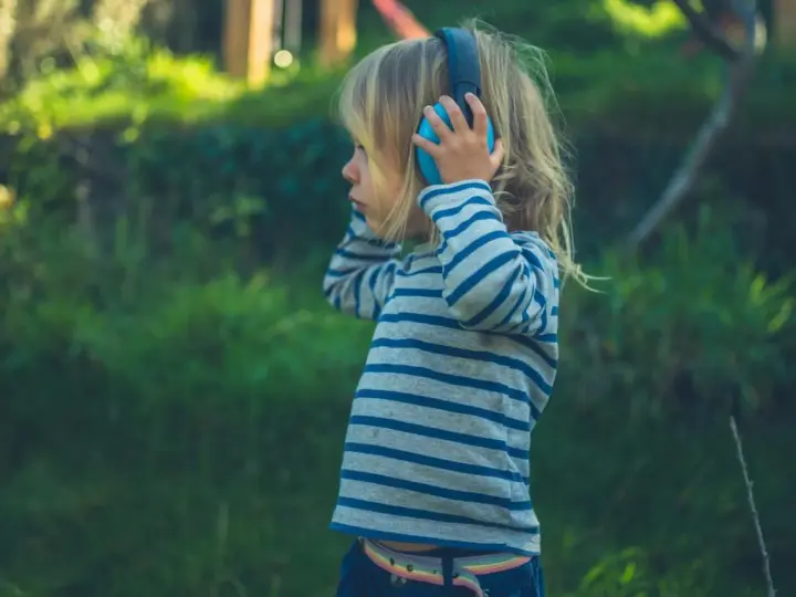 Ein Kind mit Kopfhörern im Freien, das die Welt der Klänge entdeckt. Diese Szene zeigt die Reizoffenheit bei Kindern, die sich neugierig auf neue Erfahrungen einlassen.