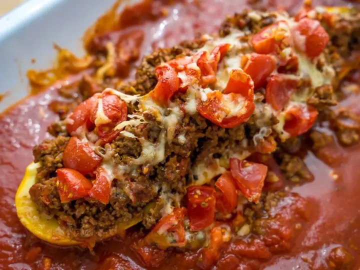 Herzhafte zucchini schiffchen gefüllt mit Hackfleisch, Tomaten und Käse, in einer aromatischen Tomatensauce.
