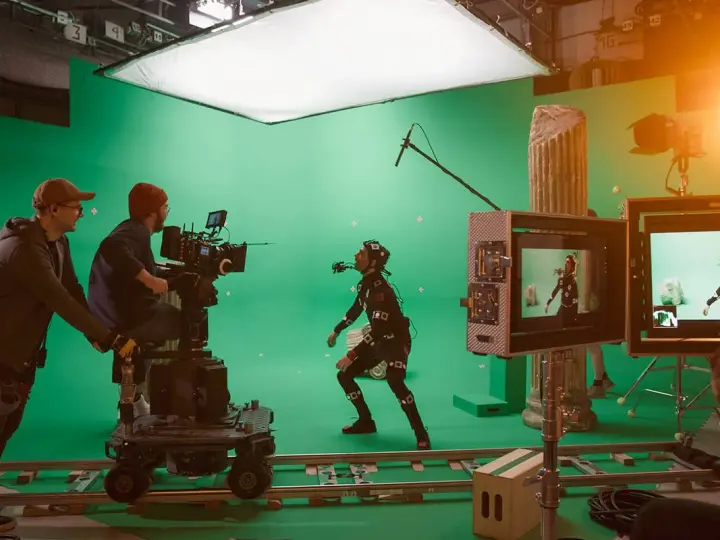 En un set de filmación con pantalla verde, un actor con traje de captura de movimiento interactúa con un equipo de filmación. Esto es vfx que es, la magia del cine.