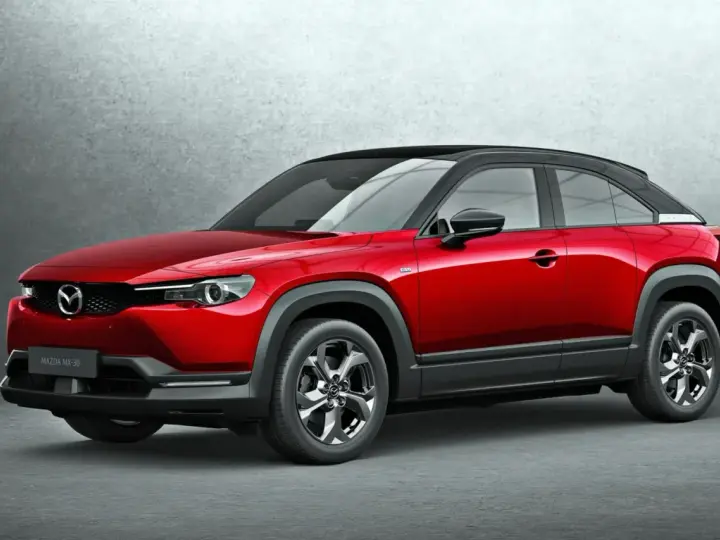 Czerwona Mazda MX-30 z czarnym dachem prezentuje się stylowo na tle szarej ściany.