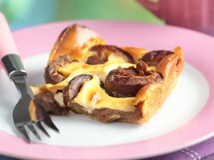 Tranche de clafoutis aux prunes moelleux sur une assiette rose avec une fourchette.