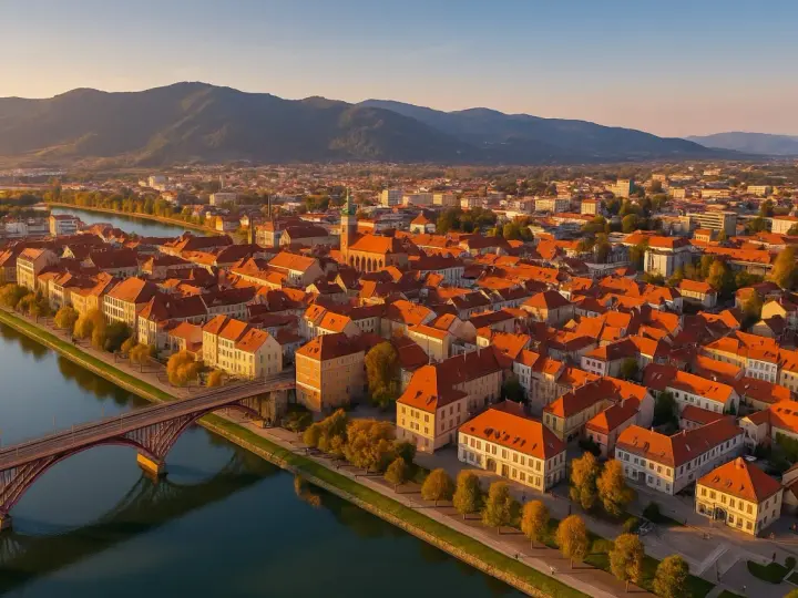 Widok na Maribor z lotu ptaka: rzeka Drava, most, zabytkowe kamienice z czerwonymi dachami i wzgórza w tle. Odkryj mariborskie atrakcje!