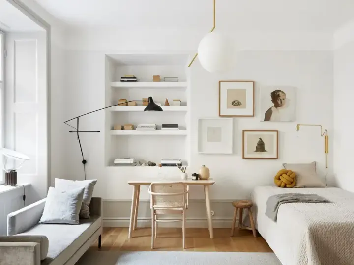 Accogliente camera da letto minimal con letto singolo, scrivania in legno, divanetto e quadri alle pareti.