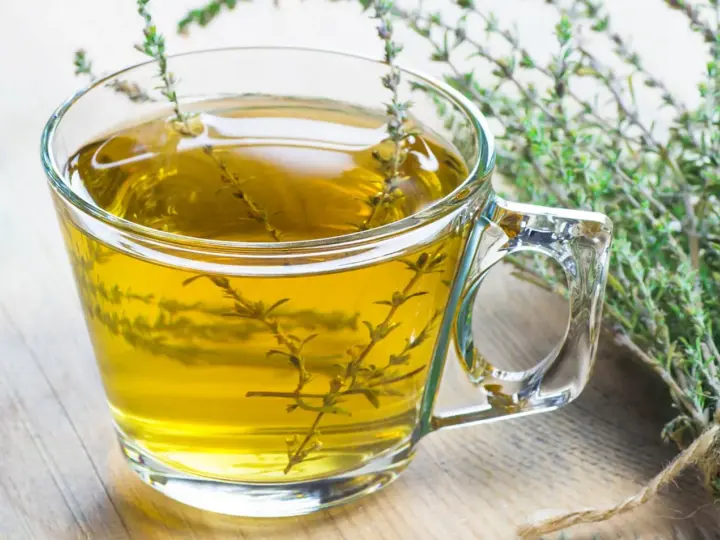 Ein Glas mit goldenem Thymiantee, daneben ein Bund frischer Thymian. Man kann den Thymian roh essen, aber Tee ist auch lecker.