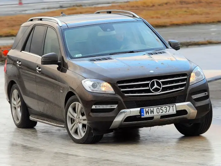 Brązowy Mercedes-Benz ML na mokrej nawierzchni, z widoczną tablicą rejestracyjną WW 0537T.