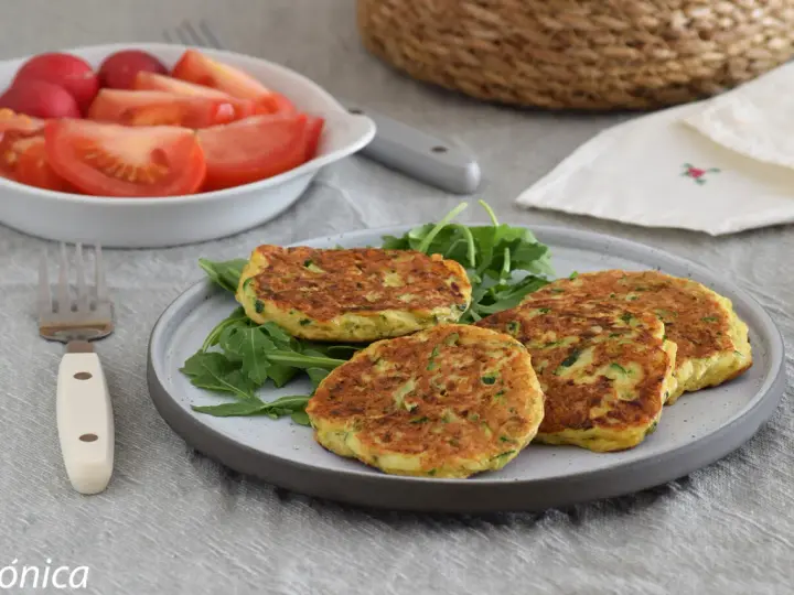 Tortitas de calabacín doradas y esponjosas, servidas sobre rúcula fresca. Acompañadas de una ensalada de tomate y rábano.