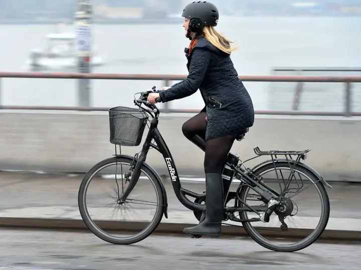 Kvinna cyklar på en elcykel, kanske med bidrag för att underlätta pendlingen. Hon bär hjälm och en varm jacka.