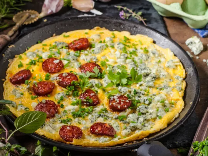 Pyszny omlet na słono z kawałkami chorizo i niebieskim serem, posypany szczypiorkiem i natką pietruszki.