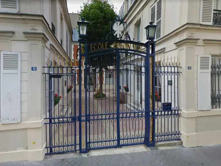 Brama do Ecole de Paris, ozdobiona złotymi detalami, prowadzi na dziedziniec z drzewem i ławką.