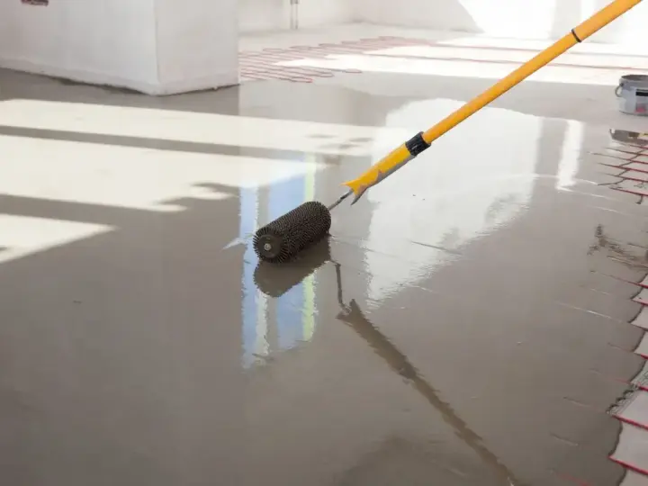 Wałek do betonu wygładzający świeżą wylewkę na podłodze z ogrzewaniem podłogowym.