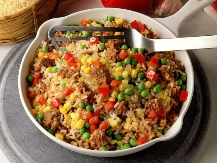 Reis mit Hackfleisch, Erbsen, Mais und Paprika in einer Schüssel, serviert mit einer Gabel.