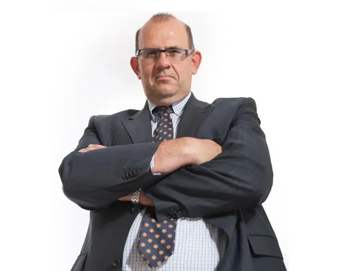 Mężczyzna w garniturze i okularach ze skrzyżowanymi rękami.