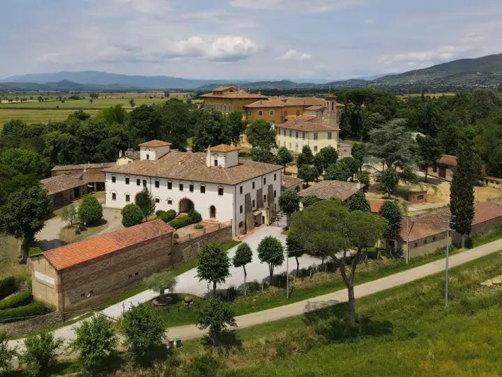 La Tenuta Frassineto, un complesso di edifici storici immerso nel verde, con campi coltivati e colline sullo sfondo.