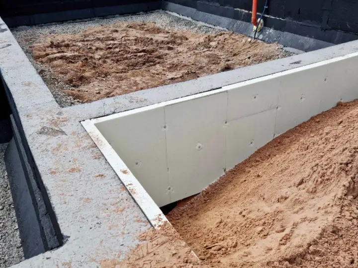 Fundament pod altanę w budowie: betonowe ławy, izolacja ze styropianu i nasypy ziemi. Słupki fundamentowe pod altanę czekają na montaż.
