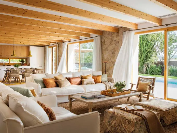 Salones blancos y madera con vigas expuestas, sofás cómodos y vistas a una piscina.