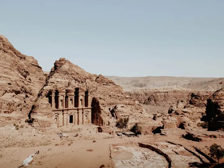 The ancient jordan ruins of Petra, carved into sandstone cliffs, stand majestically under a clear blue sky.
