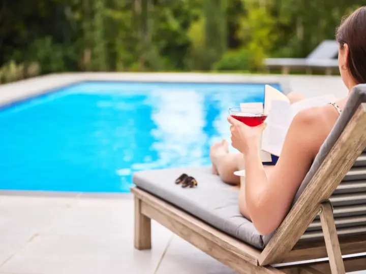Kobieta z drinkiem i książką relaksuje się przy basenie. Idealne miejsce na wakacje, łatwy kod booking.
