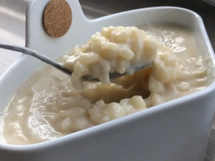 Cuillère prélevant une portion crémeuse de riz au lait dans un bol blanc.