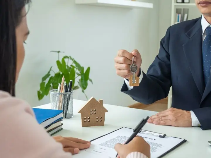 Agente inmobiliario entrega llaves a cliente. Un modelo de casa y un contrato sobre la mesa, ideal para referencia precios alquiler.