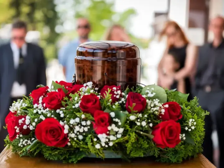 Czerwone róże i gipsówka otaczają urnę. Takie kwiaty na pogrzebie starszej osoby symbolizują miłość i pamięć.
