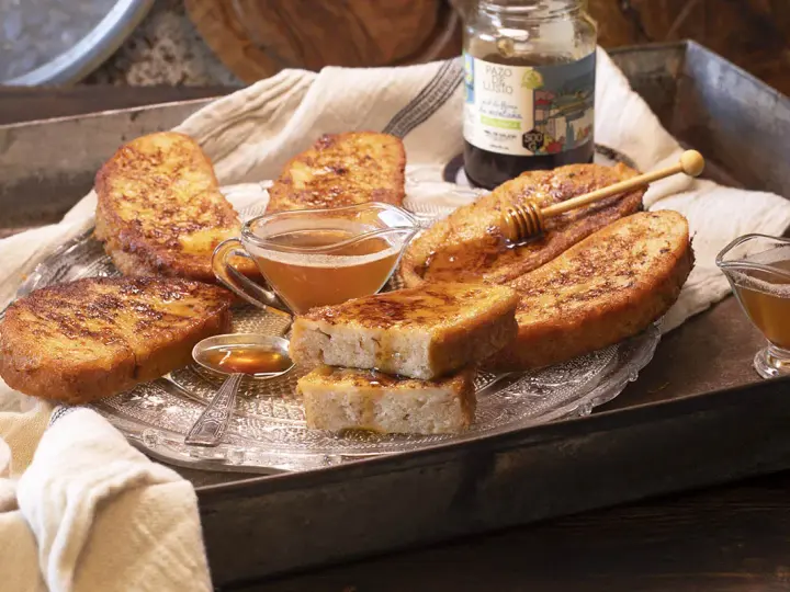 Gylla, gyllene torrejas en miel, serverade på ett fat med honung och en honungsstav.