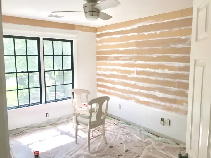 Room in progress, showing how to install shiplap on the wall. Two chairs sit on protective plastic sheeting.