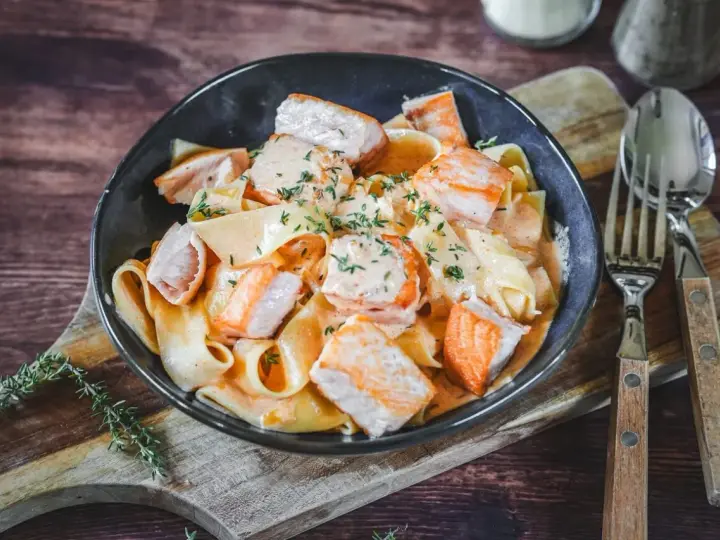 Breite Bandnudeln mit saftigen Lachs-Stücken in cremiger Lachs Sahne Sauce, garniert mit frischen Kräutern. Ein Genuss!