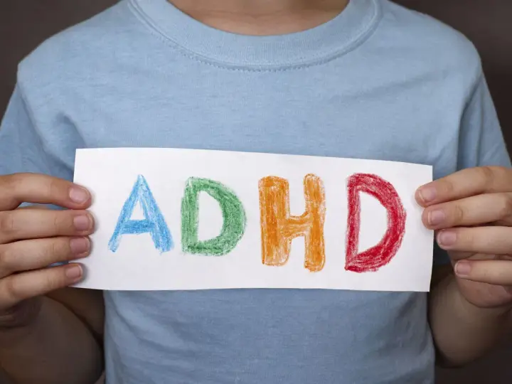 Mani di bambino tengono un foglio con la scritta "ADHD" colorata. Riconoscere i sintomi dell'ADHD è il primo passo.