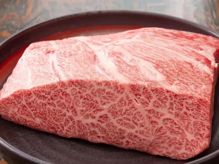 Wyjątkowy kawałek wołowiny wagyu z widocznym marmurkowym przerostem tłuszczu, prezentowany na ciemnej tacy.