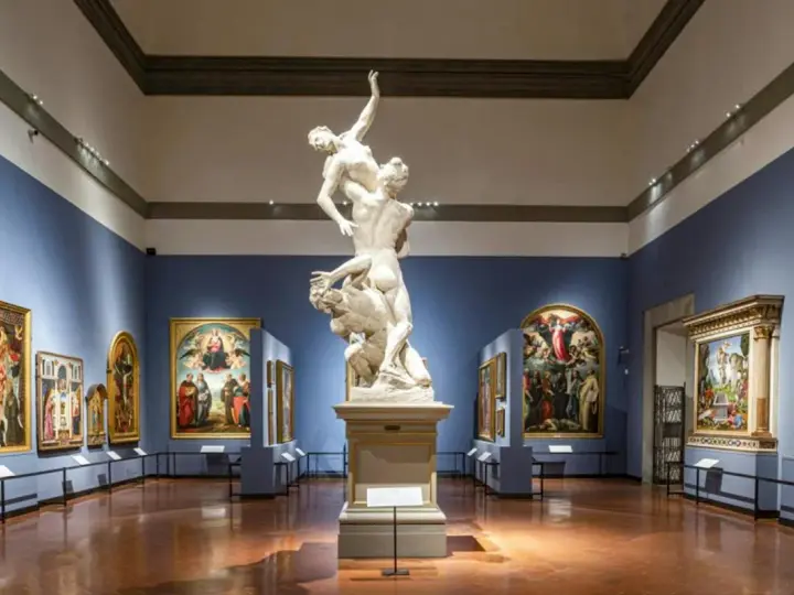 Wnętrze galerii sztuki we Florencji. Marmurowa rzeźba na piedestale, otoczona renesansowymi obrazami na niebieskich ścianach.