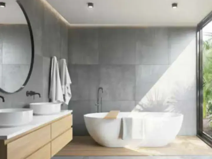 Salle de bain moderne avec baignoire îlot, double vasque et grande fenêtre donnant sur la végétation. L'étanchéité entre bac à douche et mur est assurée par des joints discrets.