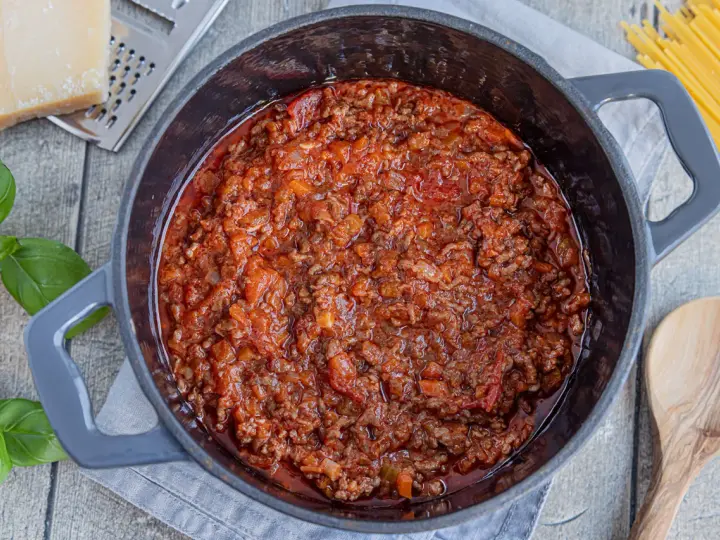 Herzhaftes Bolognese-Rezept original in einem Topf, mit frischem Basilikum, Parmesan und Spaghetti daneben.