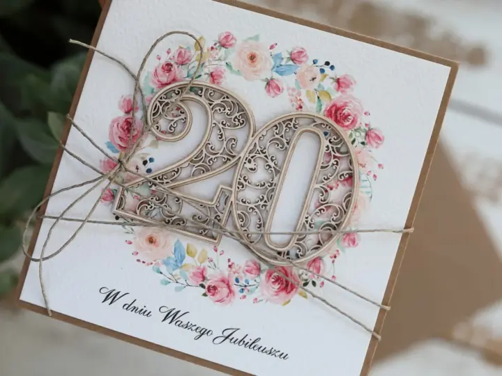 Elegancka kartka z życzeniami na 20 rocznicę ślubu, ozdobiona drewnianą cyfrą "20" i kwiatowym wiankiem.