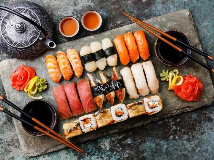 Zestaw sushi: nigiri z łososiem, krewetkami, tuńczykiem, węgorzem i rolki. Obok czajniczek, miseczki z herbatą i sos sojowy. Tak jedzą japończycy.